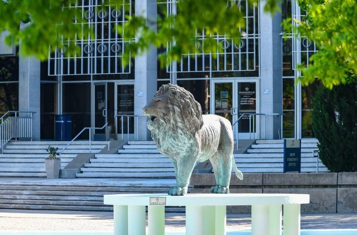 图为一所大学的建筑，前面有一尊狮子雕像